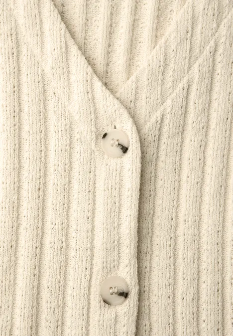 Nahaufnahme eines cremefarbenen, gerippten Strickcardigans mit großen Perlmuttknöpfen.